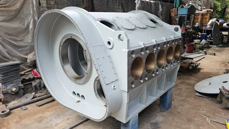 Large grey welded steel housing with a machined face holding five large bores, bolted cover plates on top and a flanged bore opening at the end